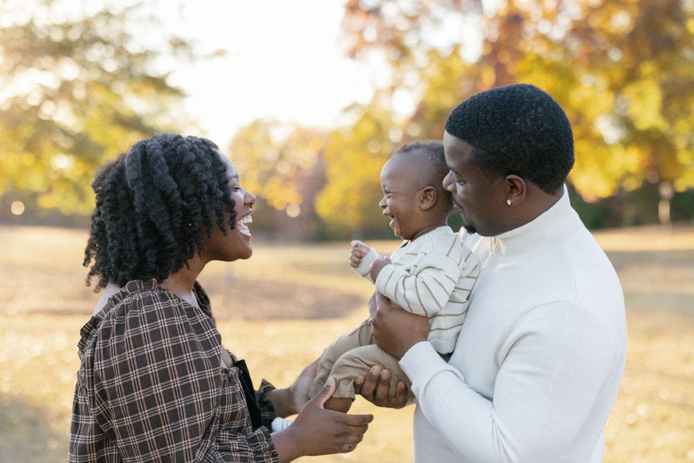 A couple shares tender moments in a park during golden hour as autumn leaves fall around them.