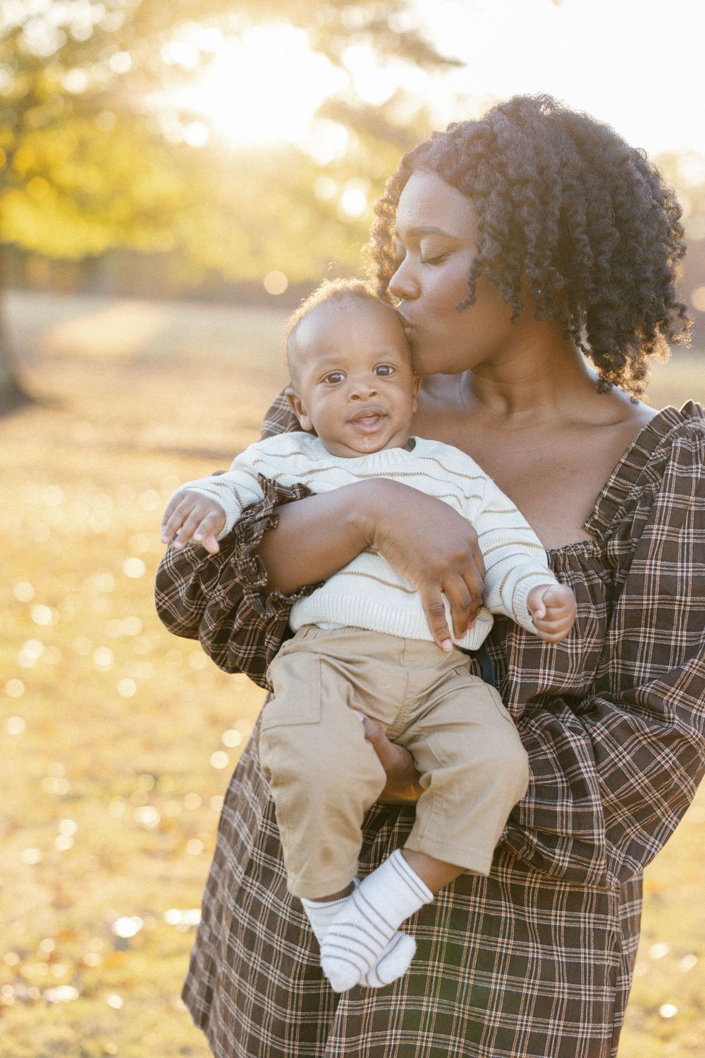 A tender family moment captured in golden sunlight with autumn leaves in the background.