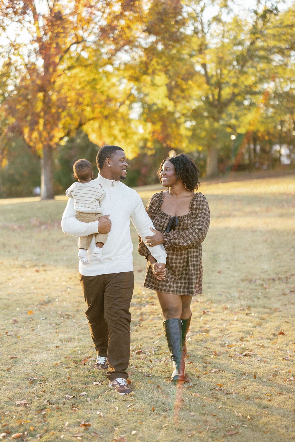 A family walks together on an autumn day with golden leaves and sunlight in the background.