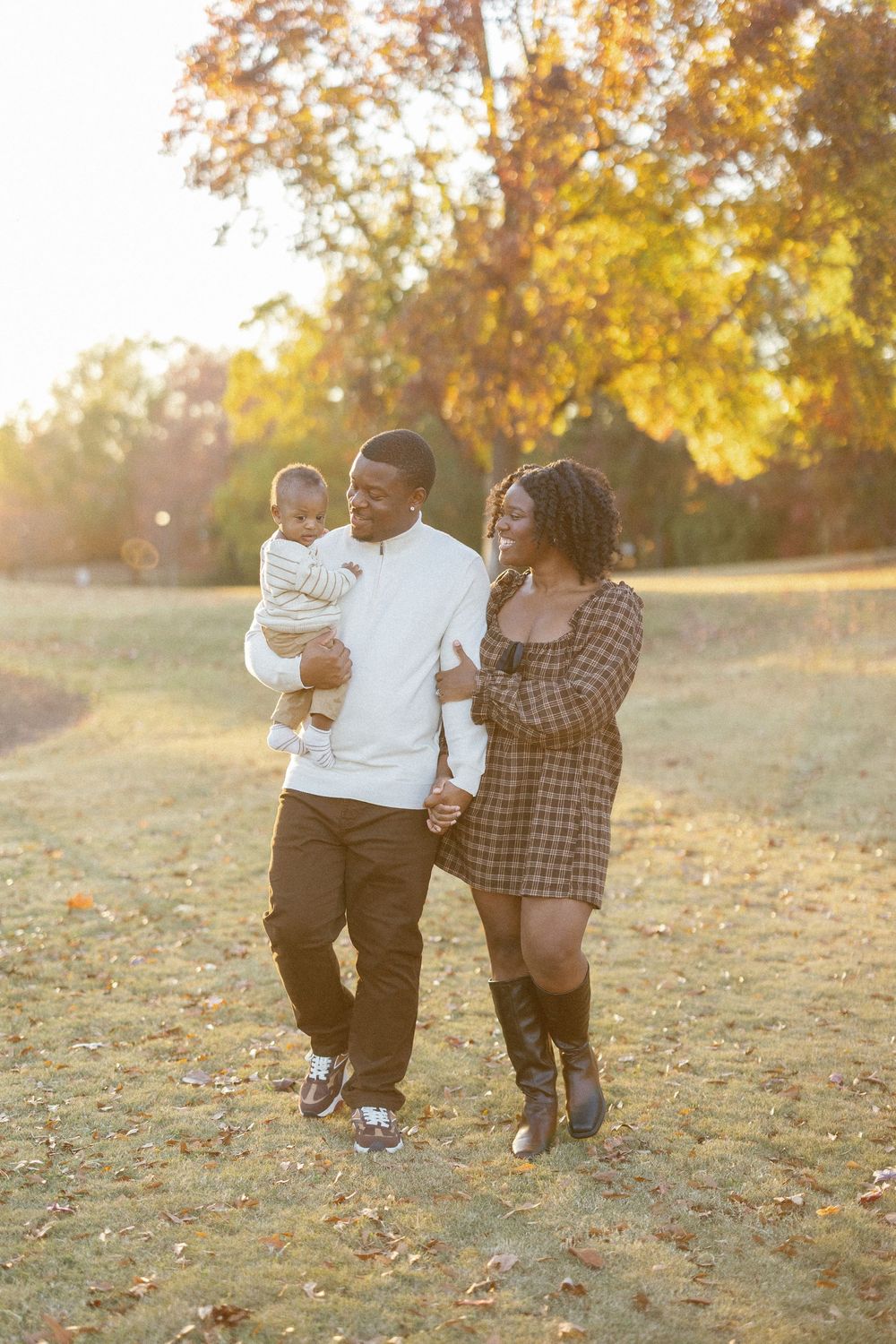 Family enjoying a tender moment together on fallen leaves during a sunny autumn afternoon.