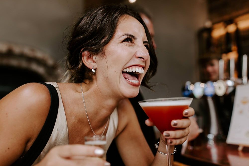 Group of friends laughing and enjoying drinks together at a bar gathering.