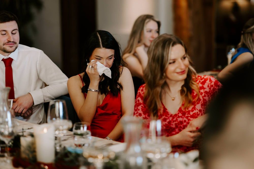 Wedding guests enjoy an elegant dinner reception at a long table decorated with floral centerpieces and candlelight.