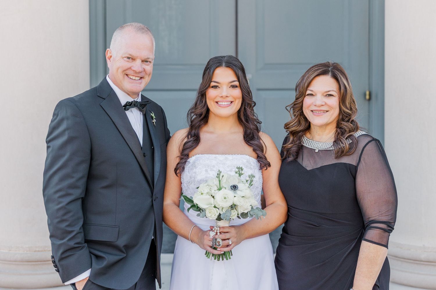 A wedding party in formal attire poses together in front of a light blue wall with white trim.
