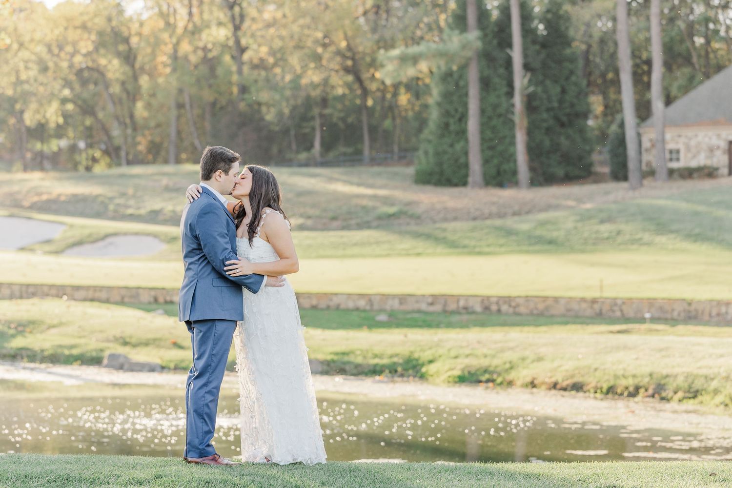 A couple in wedding attire share a romantic moment on a golf course with golden autumn light in the background.