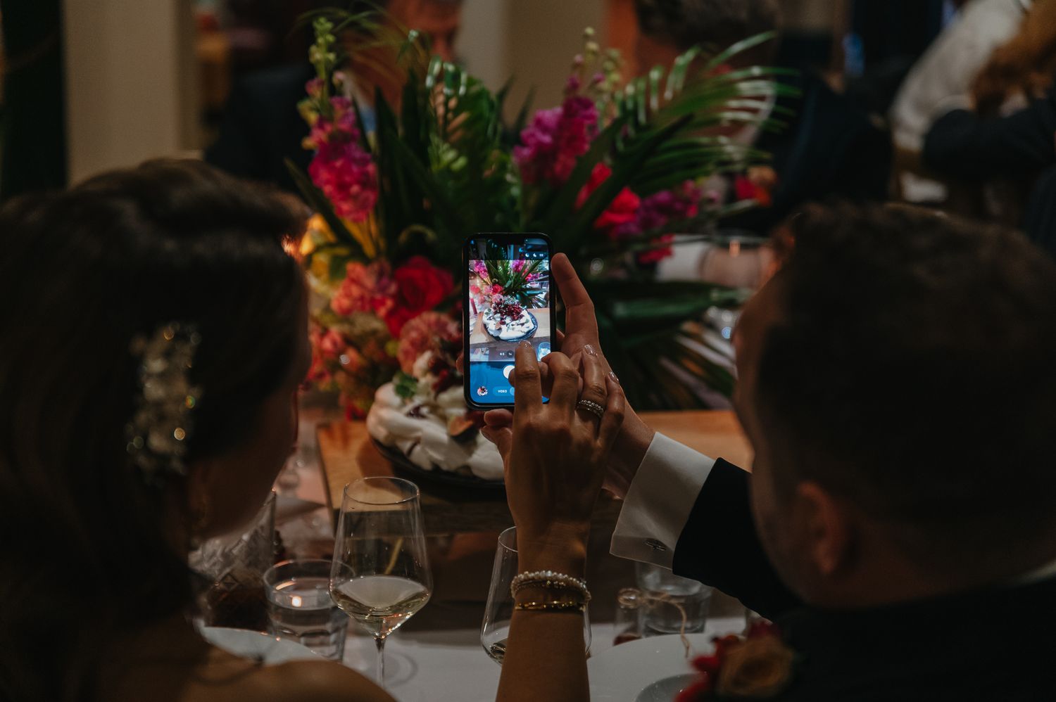 A festive wedding reception table setting with tropical flowers and elegant glassware in warm lighting.