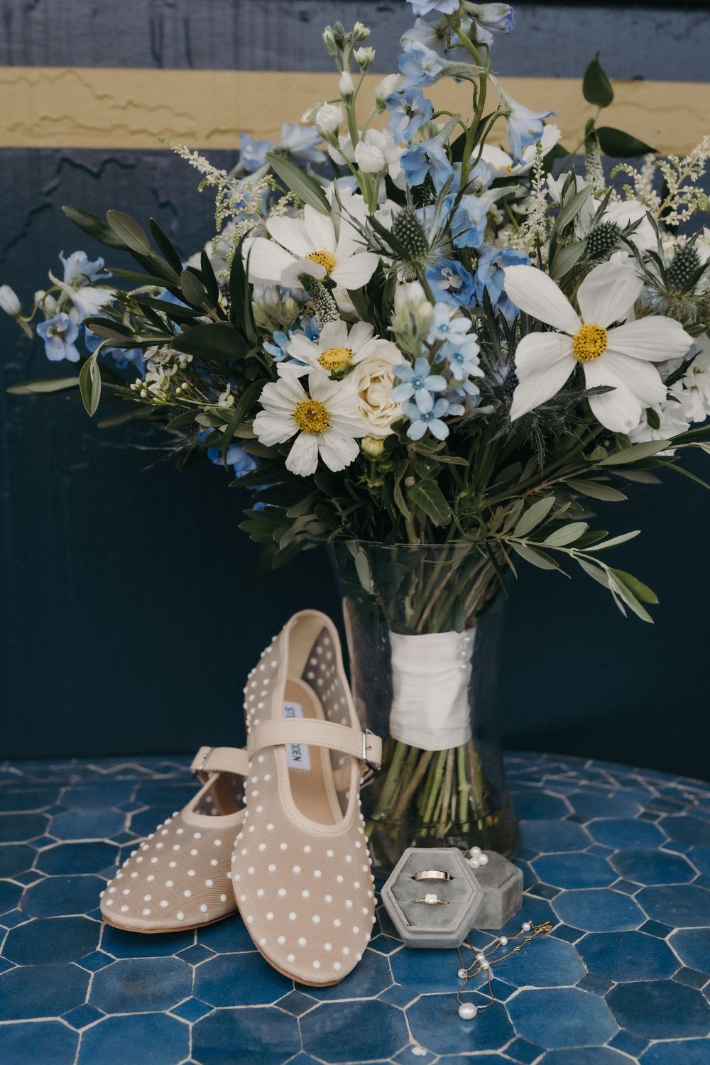 Delicate white floral arrangements with daisies and baby's breath displayed next to polka dot shoes on blue tile.