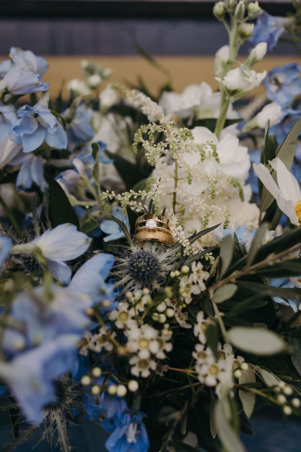 Close-up of delicate white and blue wedding flowers with rings nestled among the blooms.