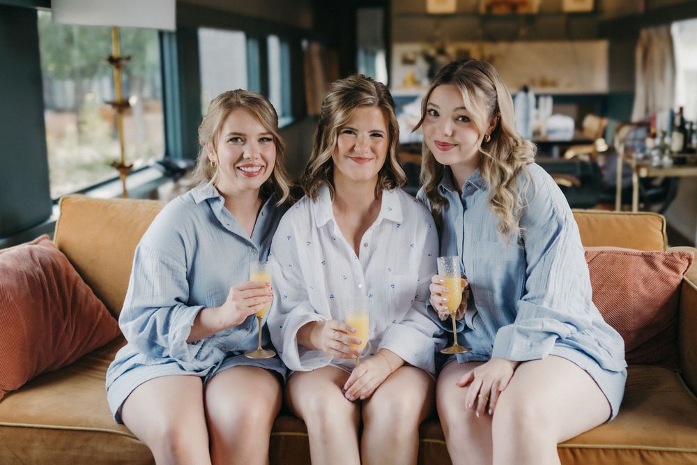 Three women in matching blue button-down shirts sitting together on a brown couch.