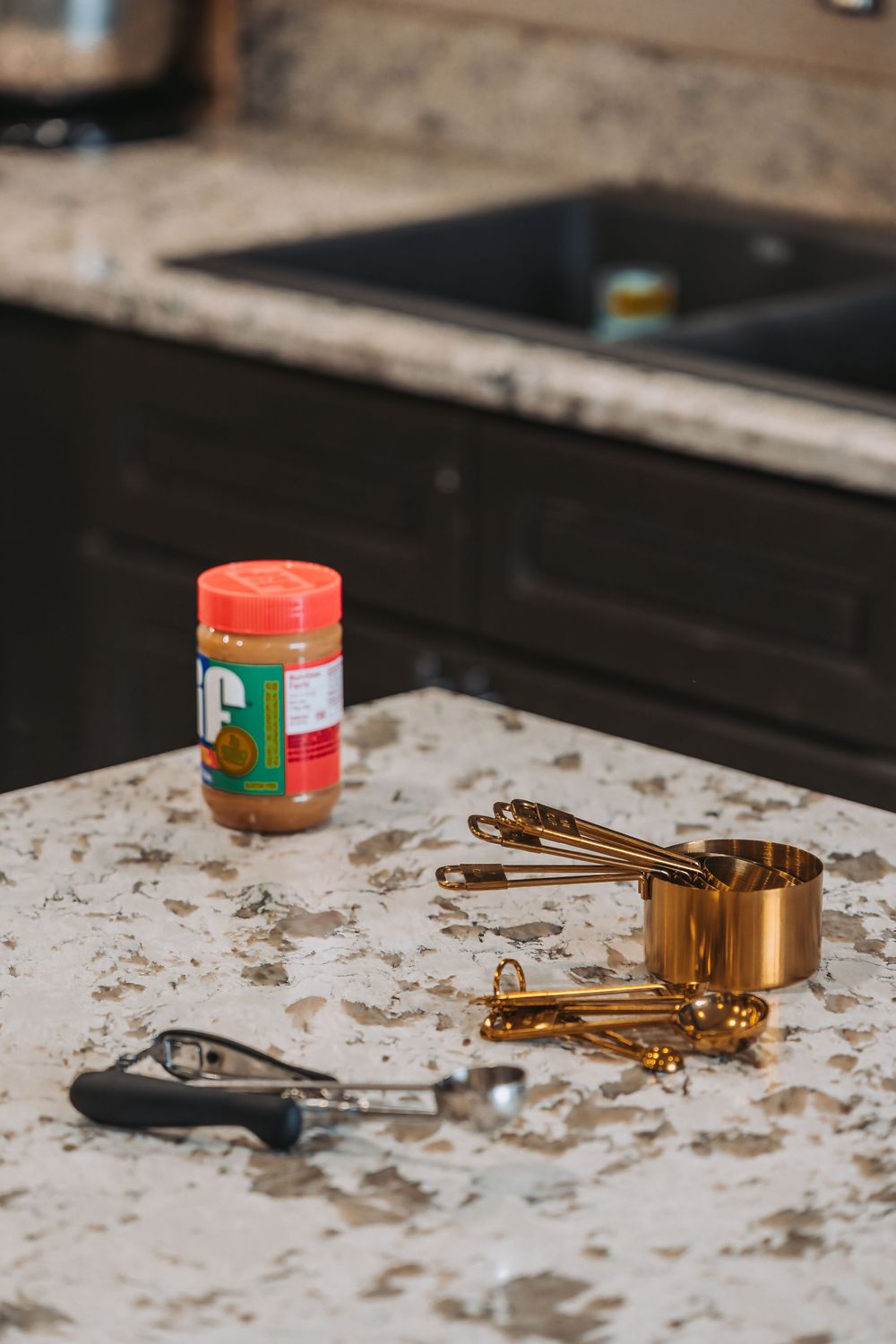 Copper measuring cups and kitchen tools rest on a marble countertop next to a jar of seasoning.