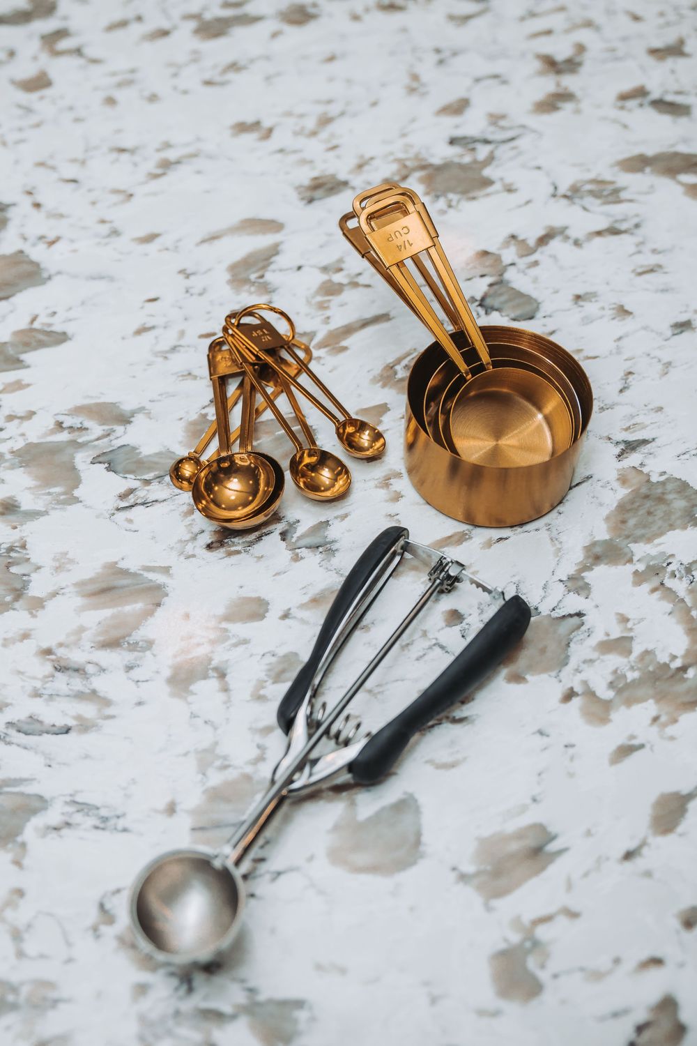 Gold and silver measuring spoons arranged on a white marble surface showcase elegant kitchen utensils and baking tools.