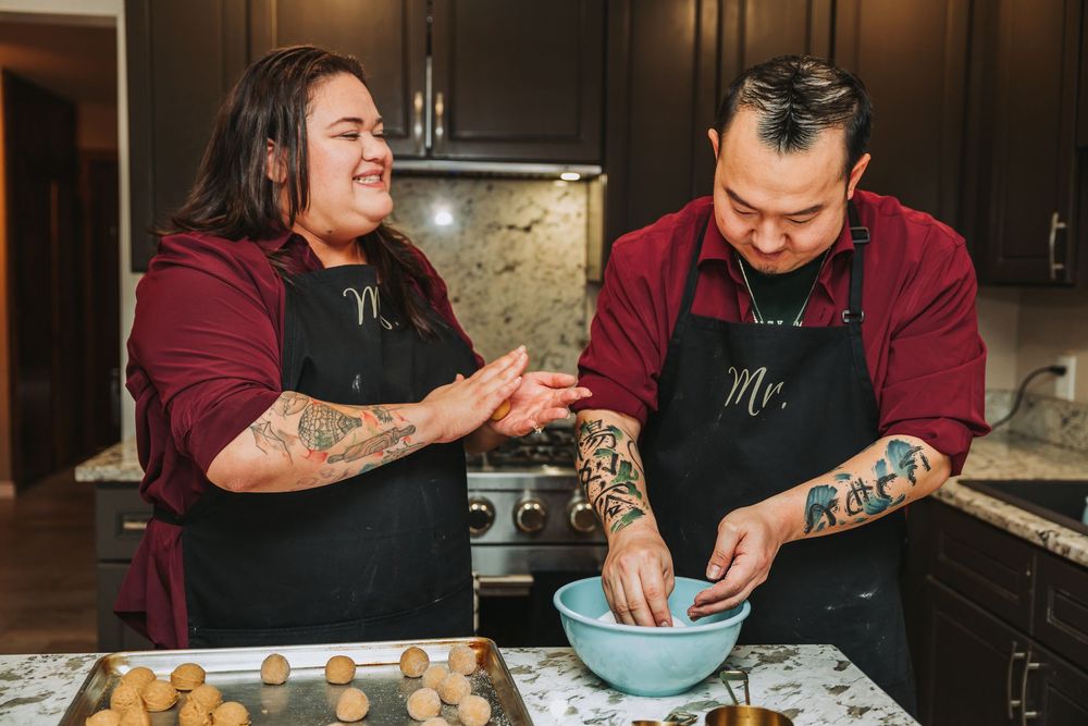 Two chefs working together in a professional kitchen preparing ingredients in a large blue mixing bowl.