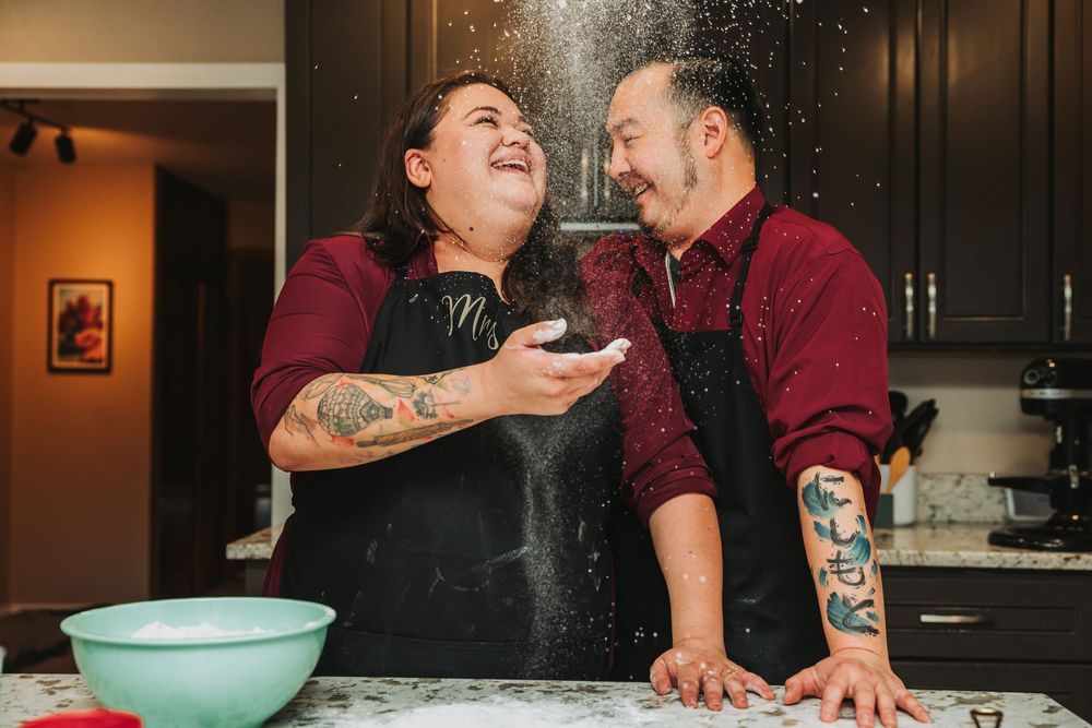 Two people laugh and play while making a mess with flour in a kitchen during a baking session.