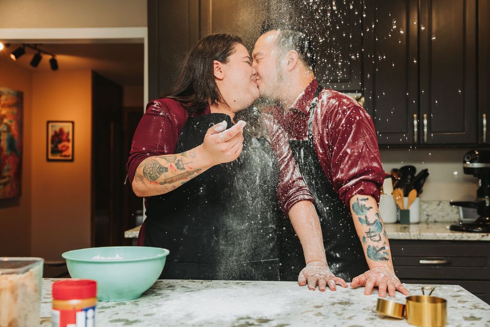 Couple playfully baking together in kitchen with flour scattered everywhere creating a messy but romantic atmosphere.