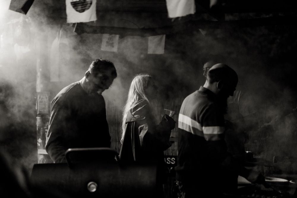 A dark and moody black and white photograph showing people standing in atmospheric smoke or fog.