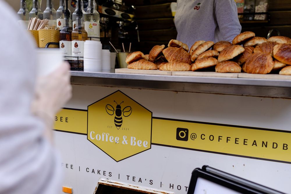 A bakery counter displays fresh bread loaves with a yellow bee logo and signage for coffee and tea service.