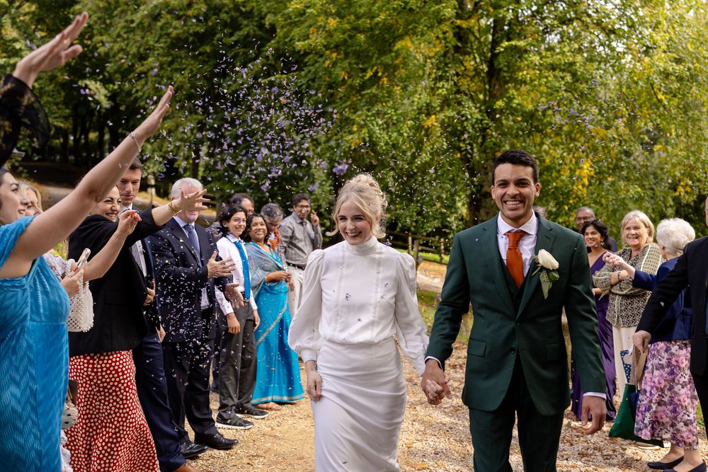 Wedding guests throw confetti and celebrate outdoors on a sunny day.