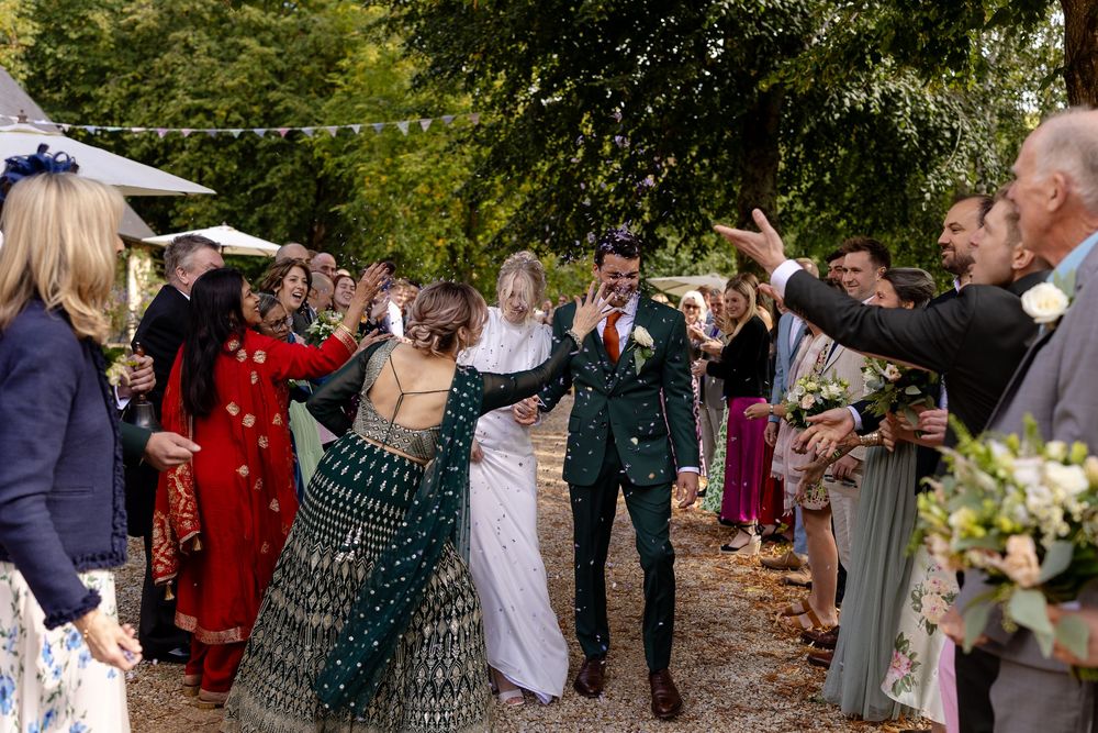 Wedding guests celebrate by throwing confetti and rice at an outdoor ceremony in a garden setting.