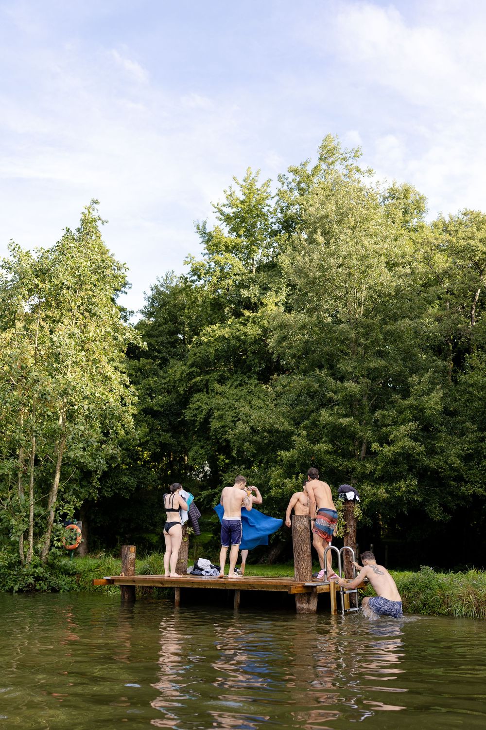People enjoying a summer day swimming and relaxing at a flooded picnic area surrounded by lush green trees.