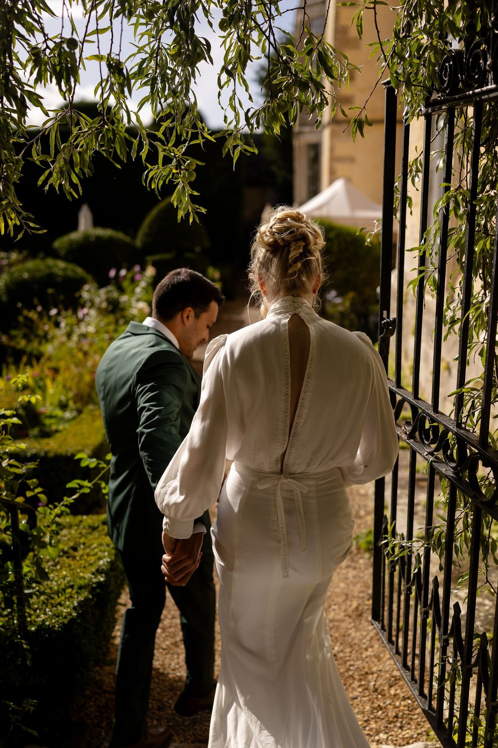 A couple walks through an ornate garden gate surrounded by hanging willow branches.