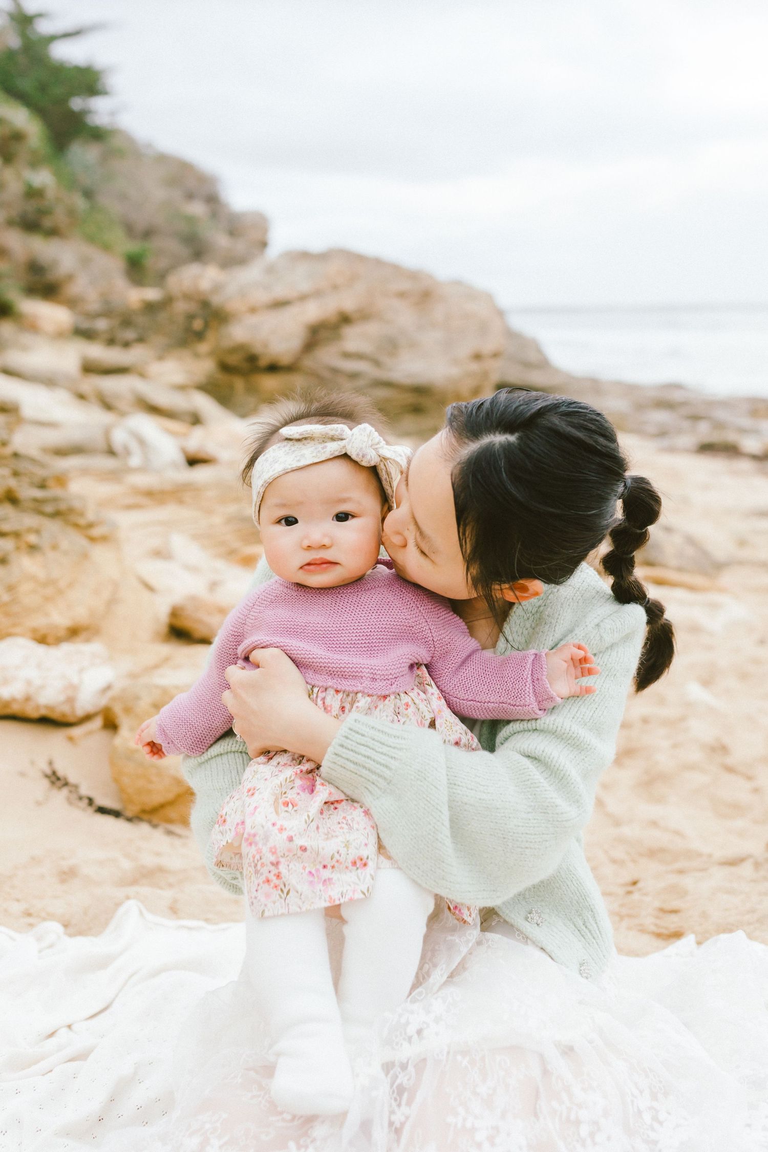 A tender moment shared between parent and child on a rocky beach with soft overcast lighting.
