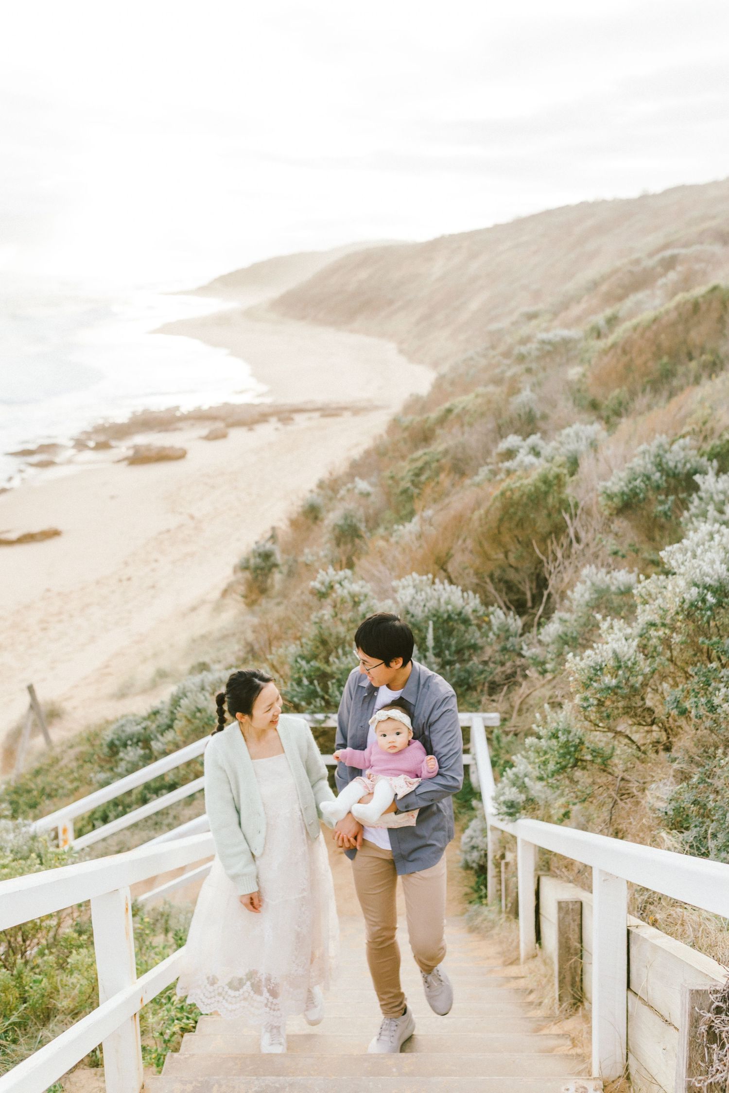 A couple walks along a scenic coastal path with white wooden railings on a misty afternoon.