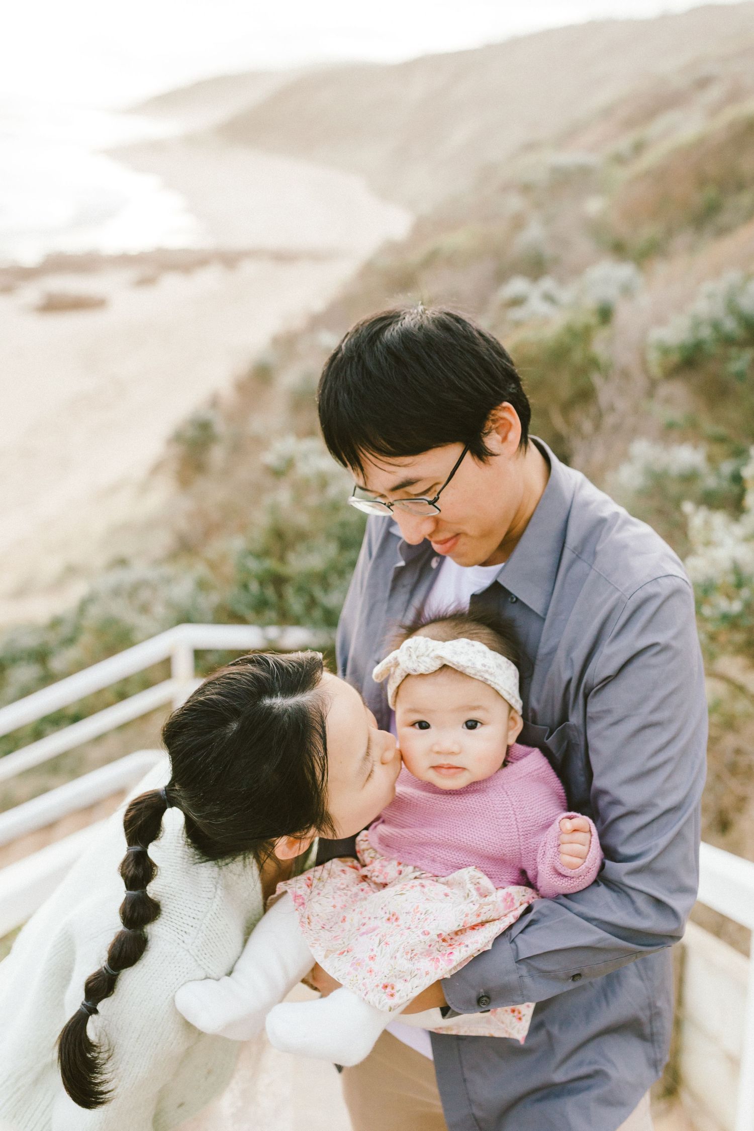 A parent in grey attire shares tender moments with a baby in pink clothing on an outdoor stairway.