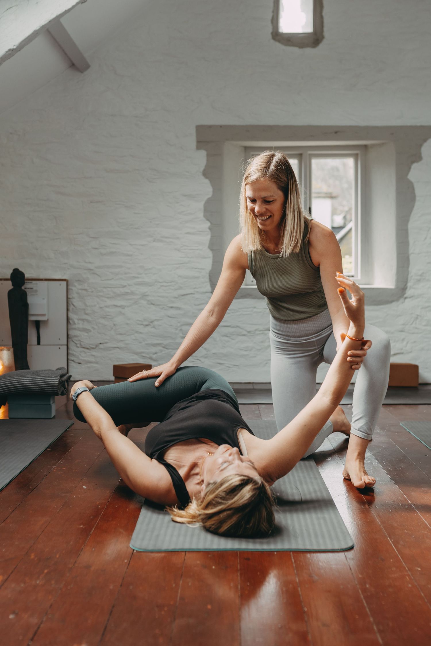 A person performs a series of stretching exercises on a yoga mat in a minimalist studio space with white walls and wooden floors.