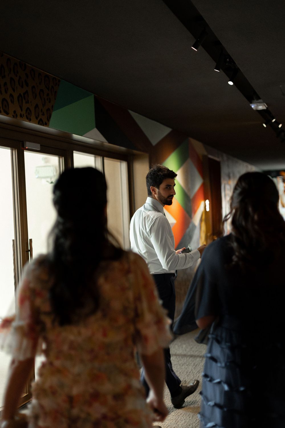 People dancing together in a dimly lit room with geometric patterns on the wall creating an atmospheric party scene.