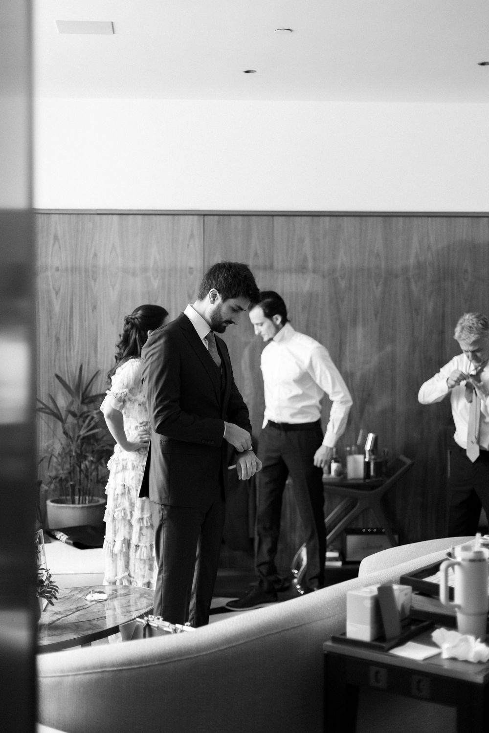 Black and white photo showing several people interacting in an office space with wood paneled walls.