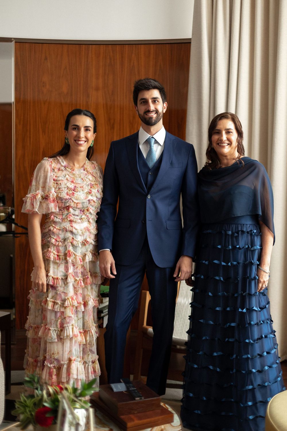 Group portrait showing formal attire with a navy suit and ruffled dresses against wood paneling and curtains.