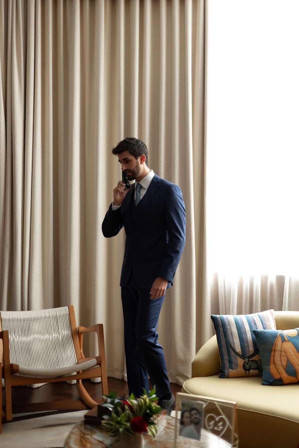 Multiple frames capture someone in a blue suit standing near beige curtains and modern furniture.