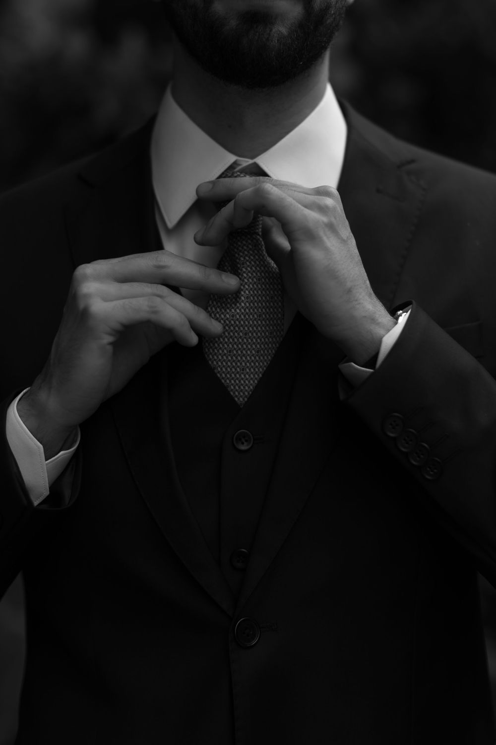 Close-up black and white photo of hands adjusting a necktie and collar.