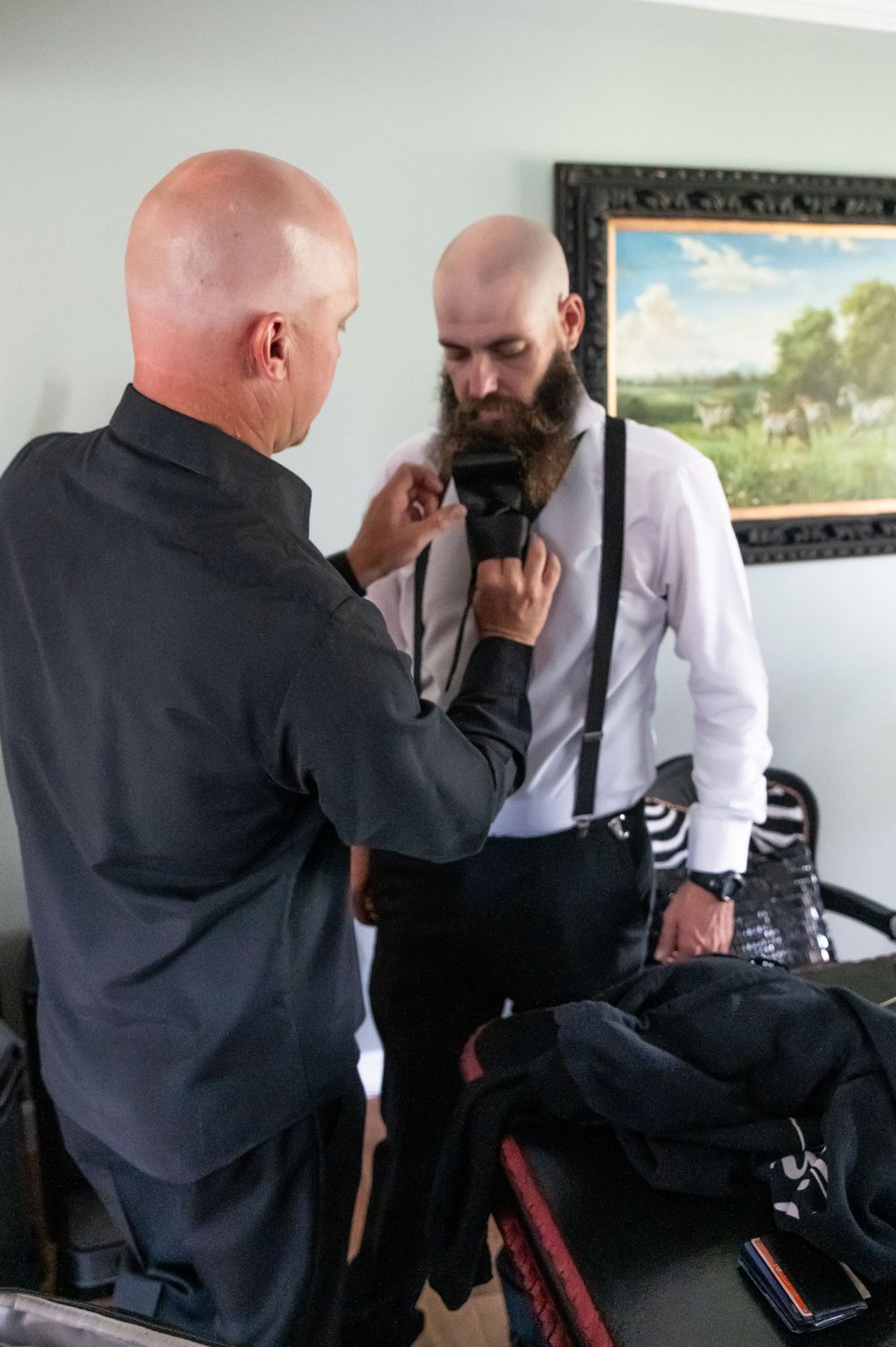 Two people in formal attire examine and light up cigars together in an indoor setting.