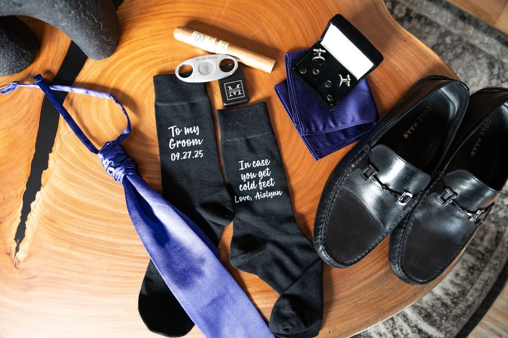 Black sneakers, socks, and accessories arranged on a wooden surface with natural lighting.