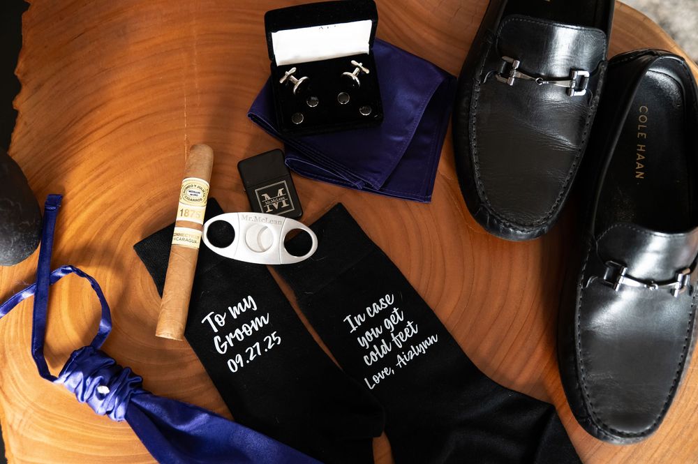 Black leather sandals with white text writing displayed on wooden surface next to coffee cup and dark objects.