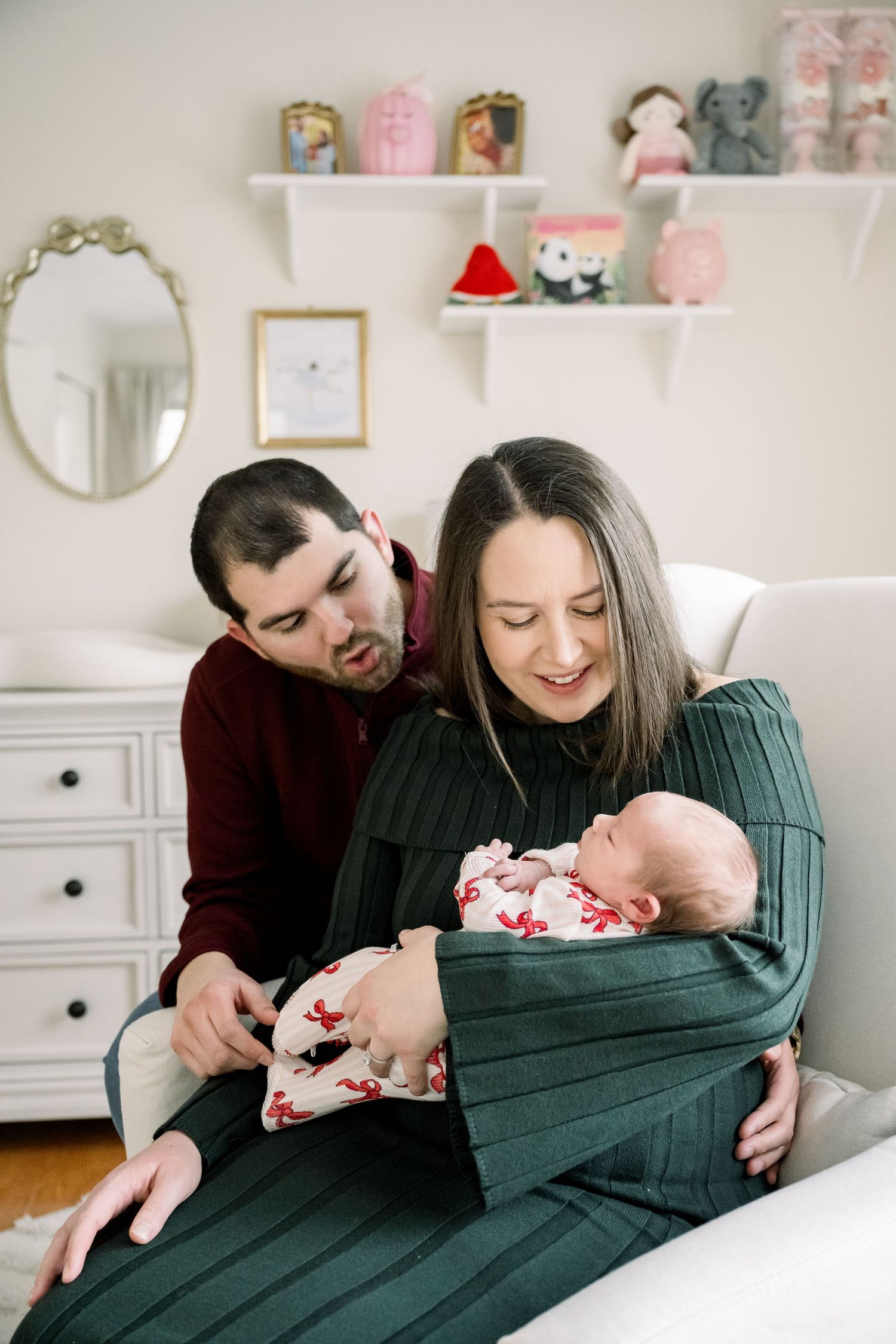 A tender family moment in a nursery room with white furniture and pink decor on floating shelves.