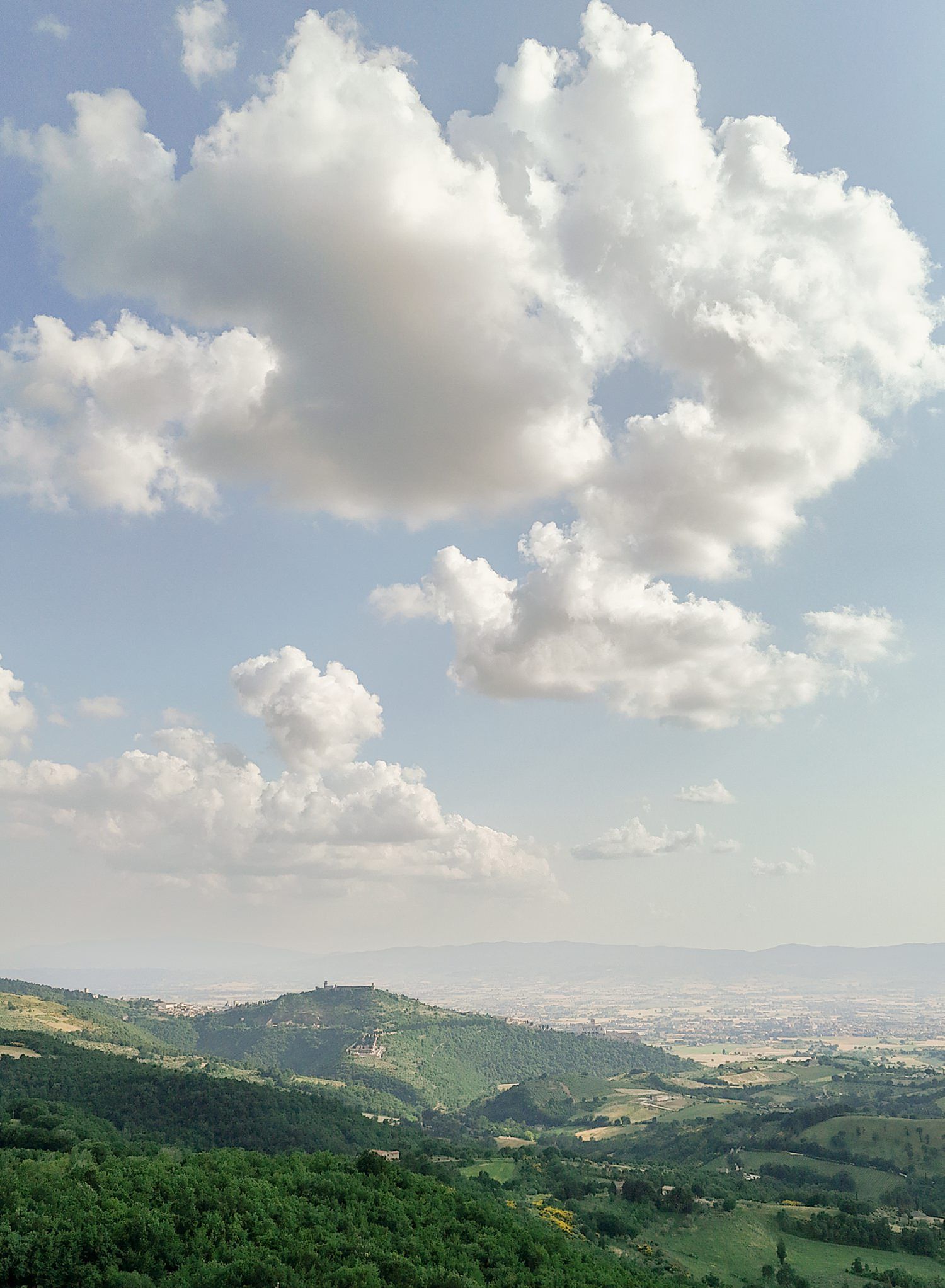 Panoramic view of rolling green hills and distant mountains under a cloudy sky with scattered white clouds.