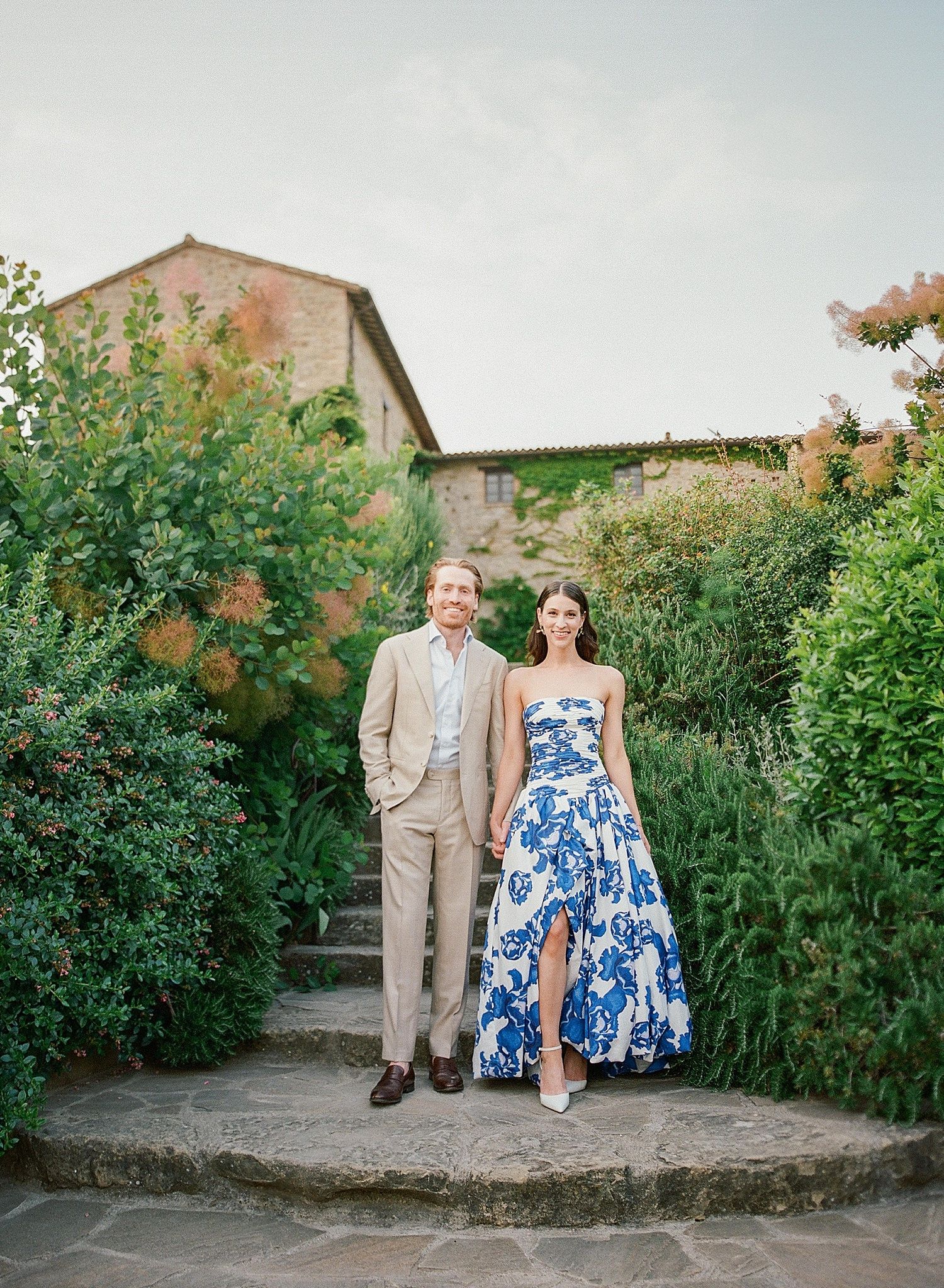 A couple in a garden setting poses for a series of romantic portraits against a stone wall and greenery.