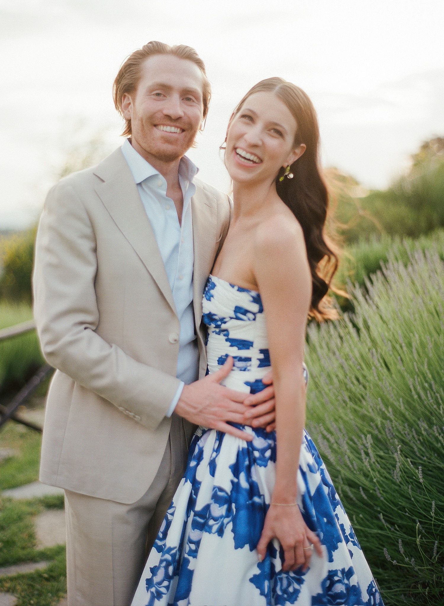 A joyful couple share a candid moment in formal attire against a backdrop of lavender plants.