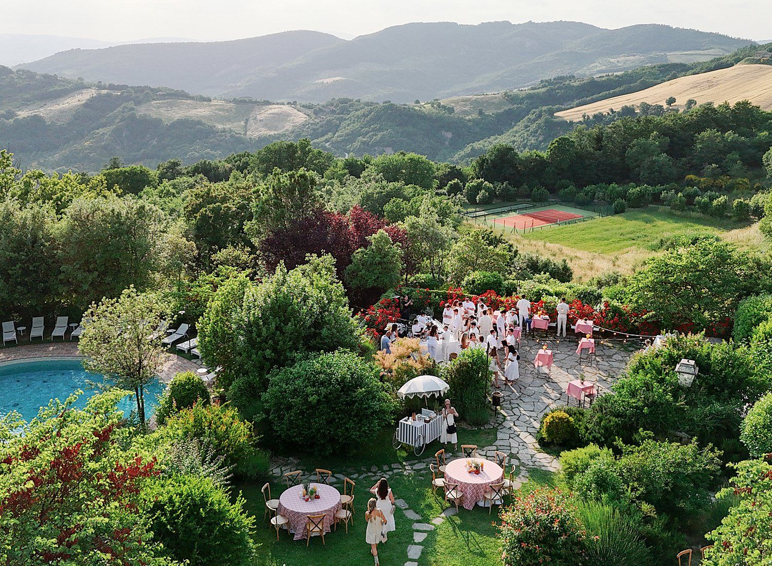 A scenic panoramic view of rolling hills and lush gardens with outdoor event tables set up for a celebration.