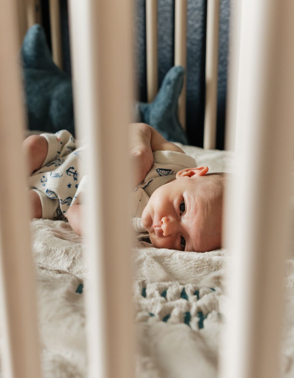 Sleeping baby in white crib viewed through slats with soft bedding.