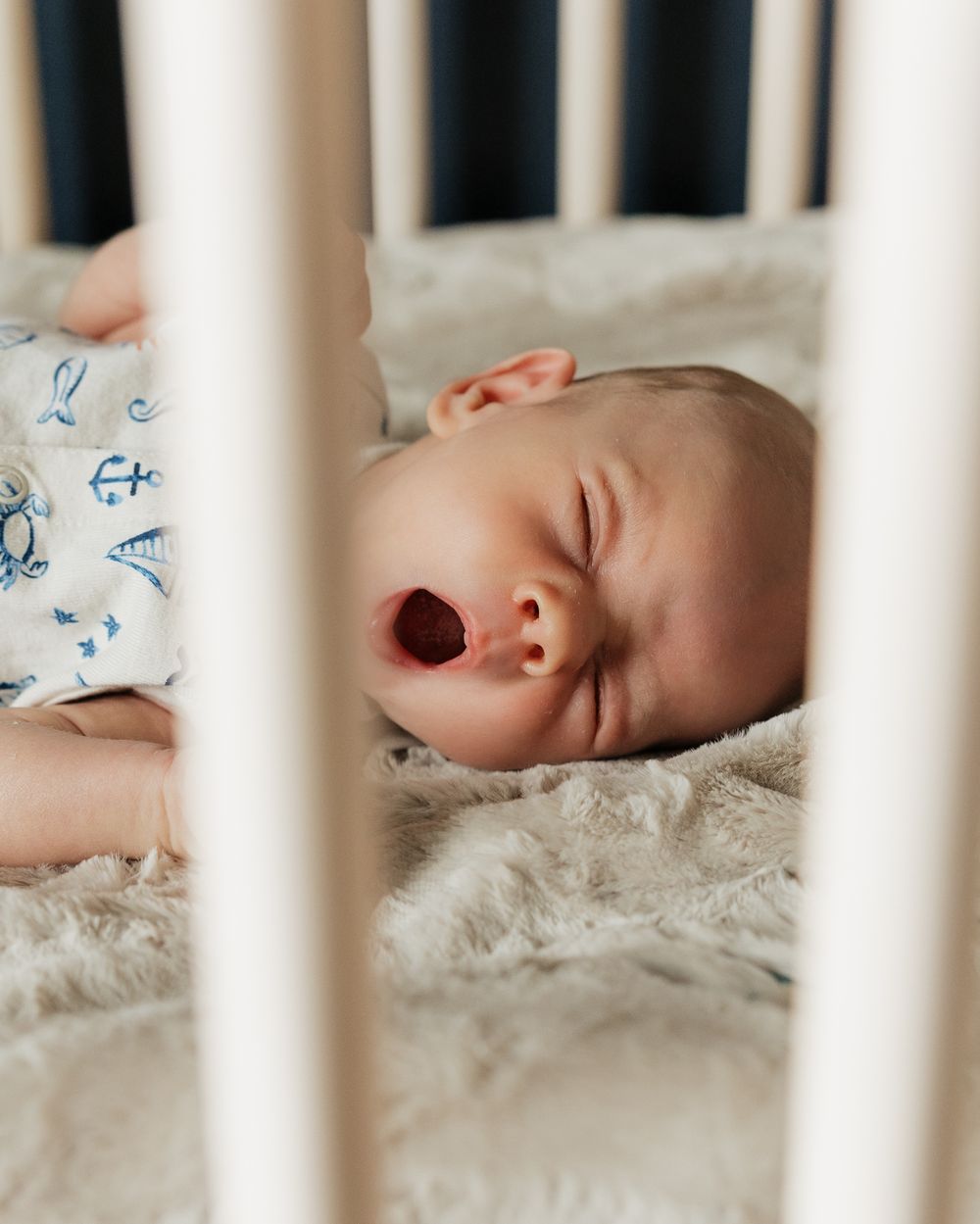Close-up of peaceful sleeping infant through white crib bars.