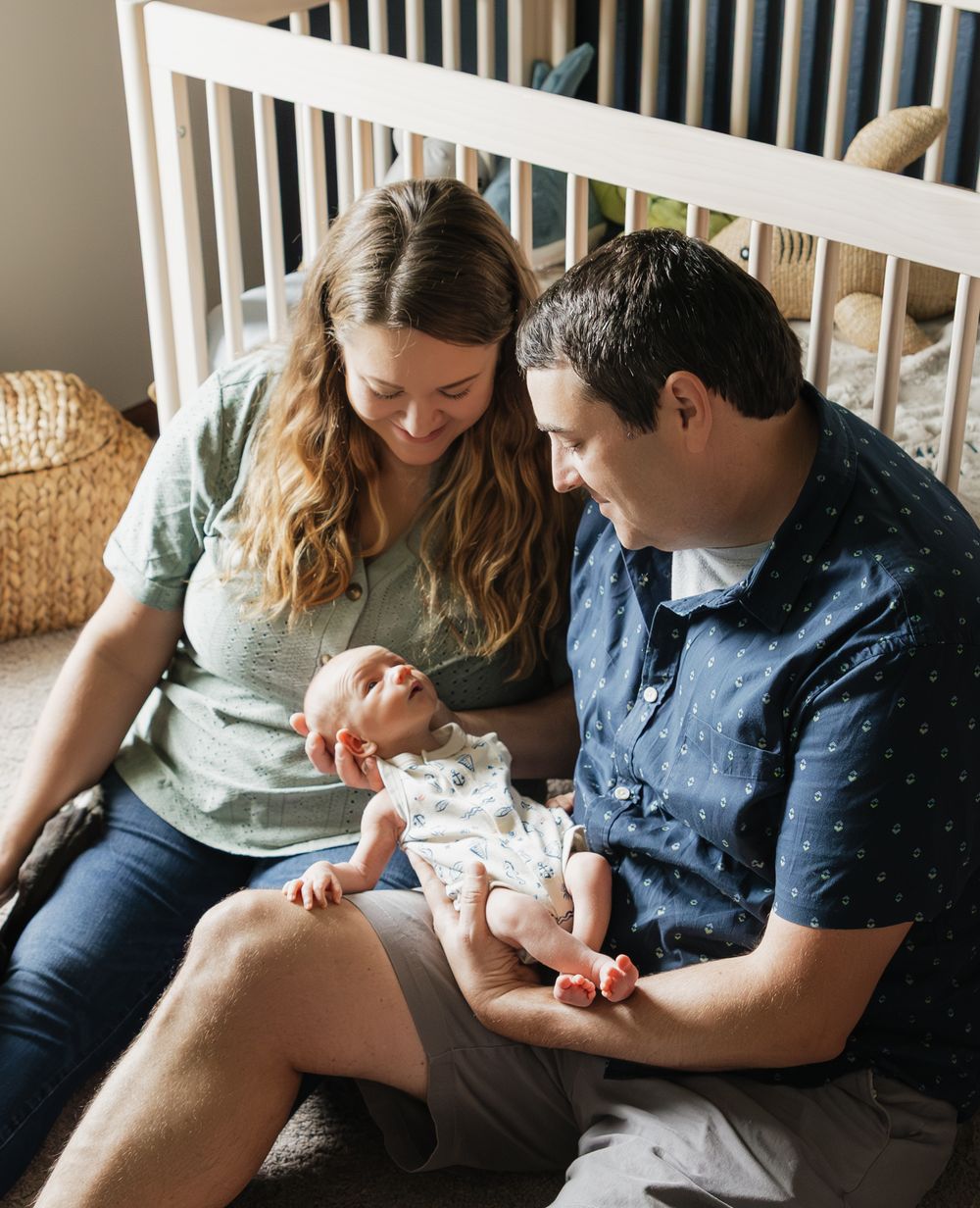 Family sharing tender moment while gathered around baby's crib.