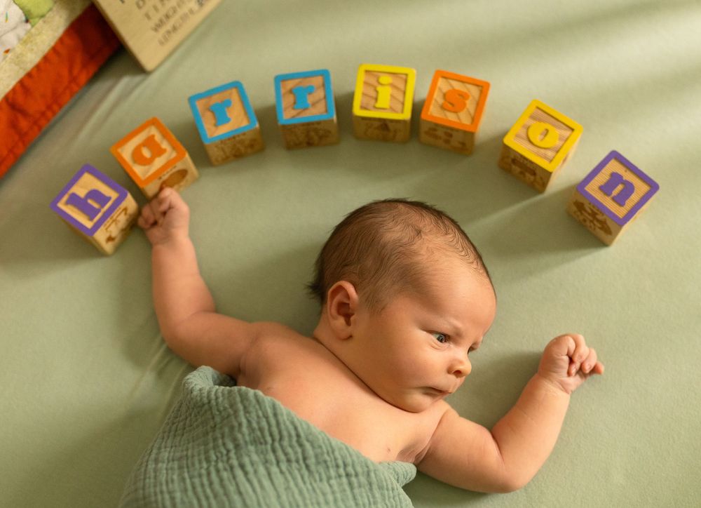 Colorful alphabet blocks line the top of a white crib where a sleeping infant rests.