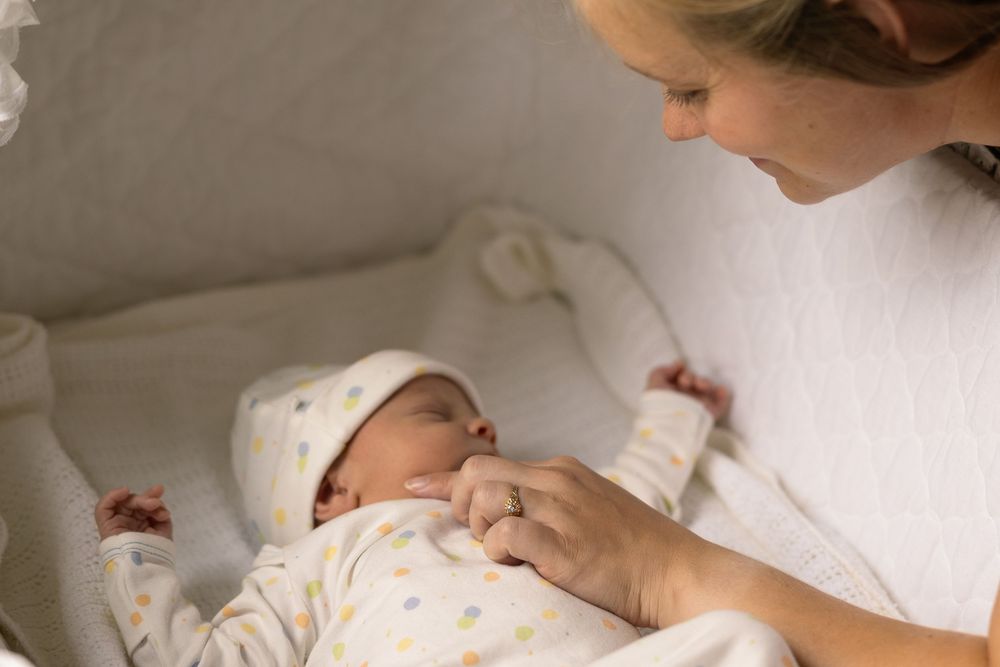 An infant sleeps peacefully in white bedding while being watched from above.