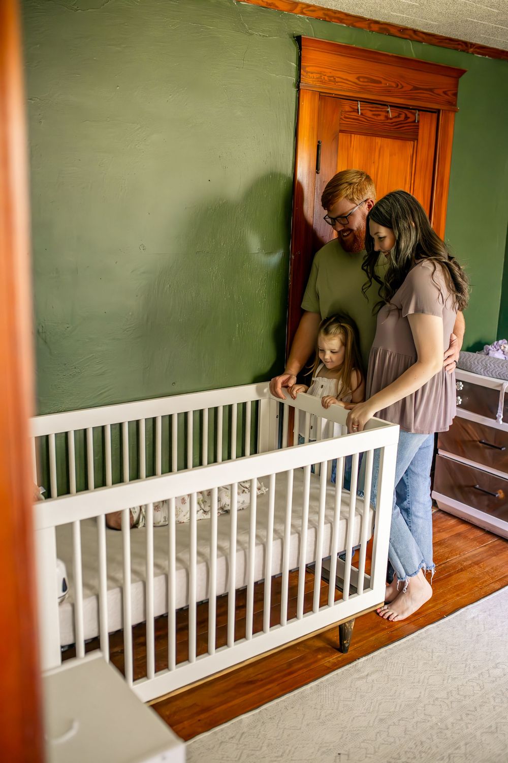 A family gathers around a white railing in a room with green walls and wooden floors.