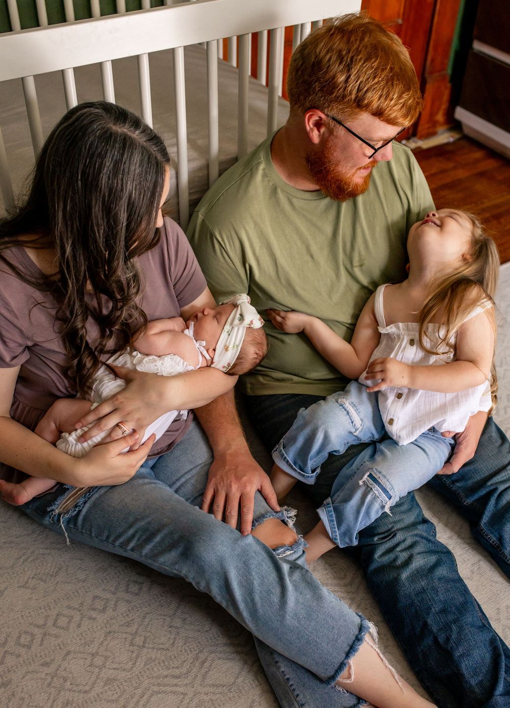A tender family moment unfolds beside a white crib in a nursery setting.