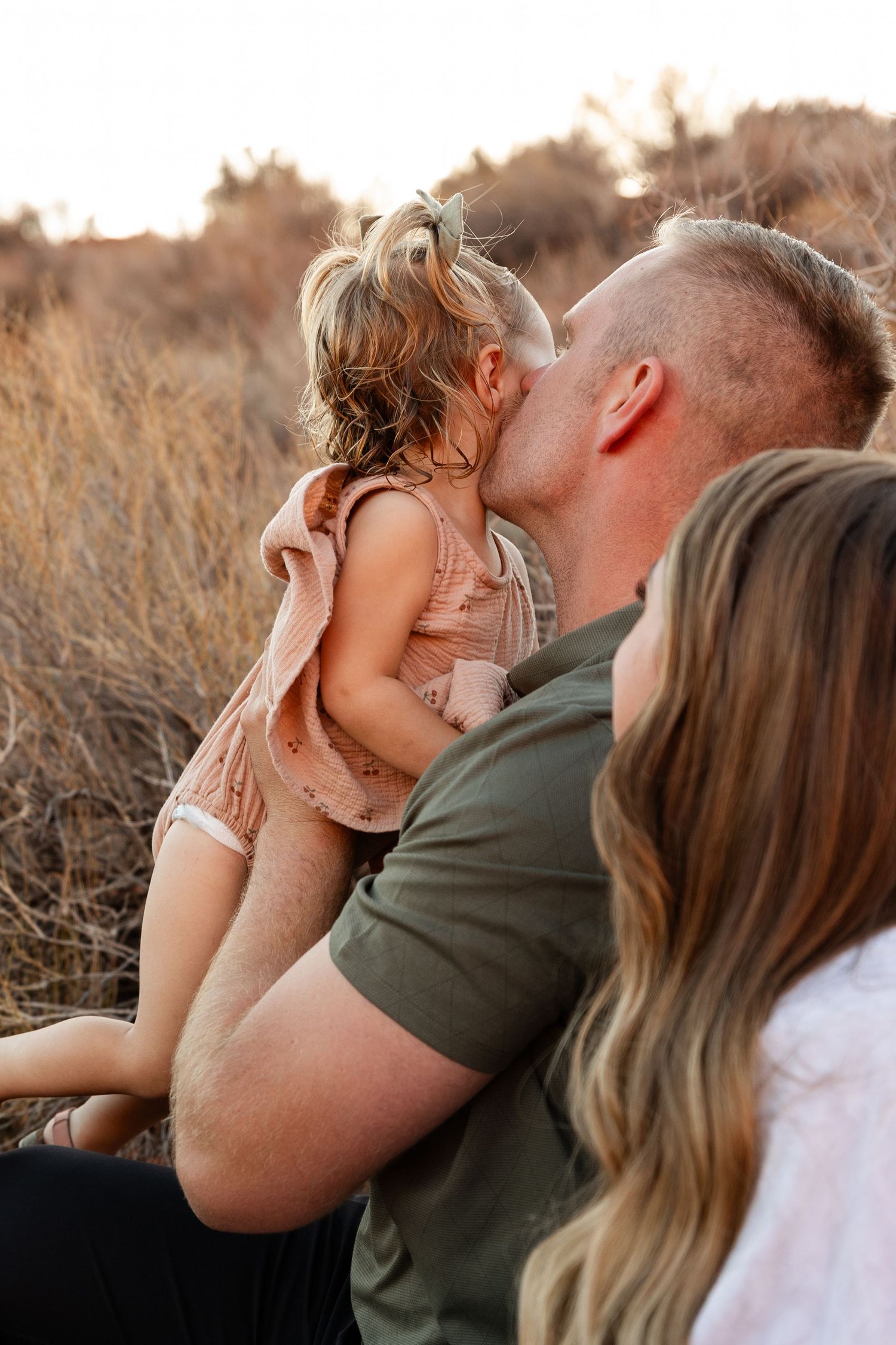 dad kissing little girls cheek with mom next to him. all turned away from the camera