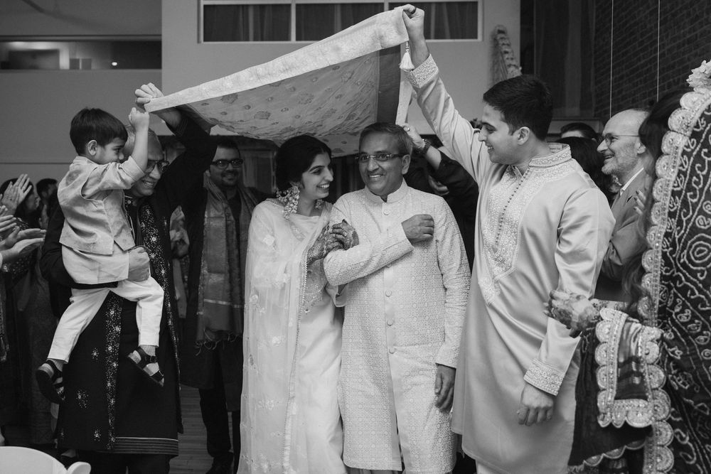 Celebratory moment at an Indian wedding with guests holding white fabric overhead.