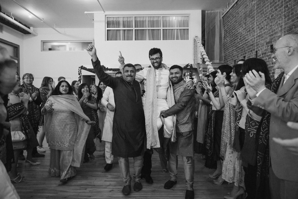 Black and white photo of joyous celebration with people dancing at an Indian wedding reception.